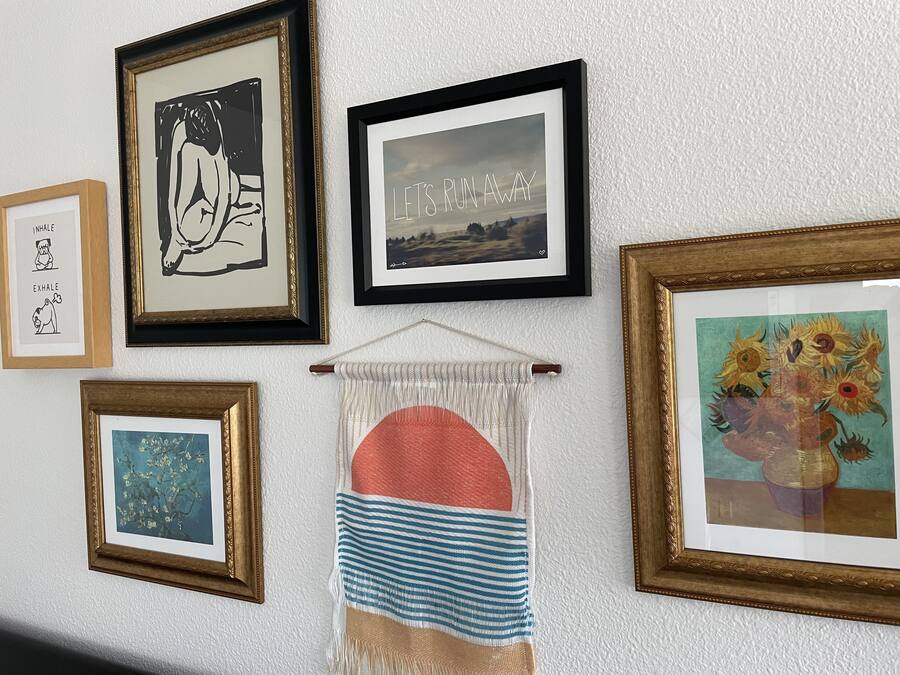 Una pared con varias obras de arte enmarcadas y una pieza de macramé.