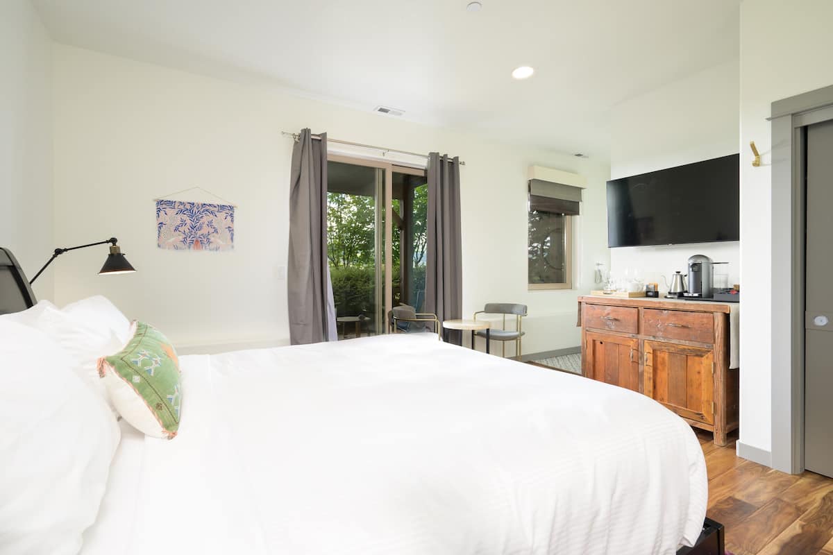 A bedroom with a large bed, a wooden dresser, a desk, and a TV mounted on the wall.