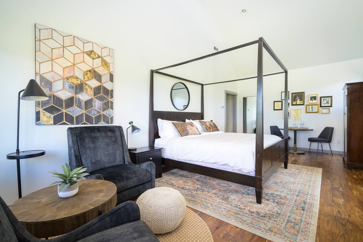 A modern bedroom with a four-poster bed, a round coffee table, a potted plant, and a decorative rug.