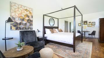 A modern bedroom with a four-poster bed, a round coffee table, a potted plant, and a decorative rug.