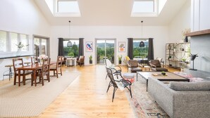 Un salon spacieux avec une table à manger en bois, des sièges confortables et de grandes fenêtres donnant sur l’extérieur.
