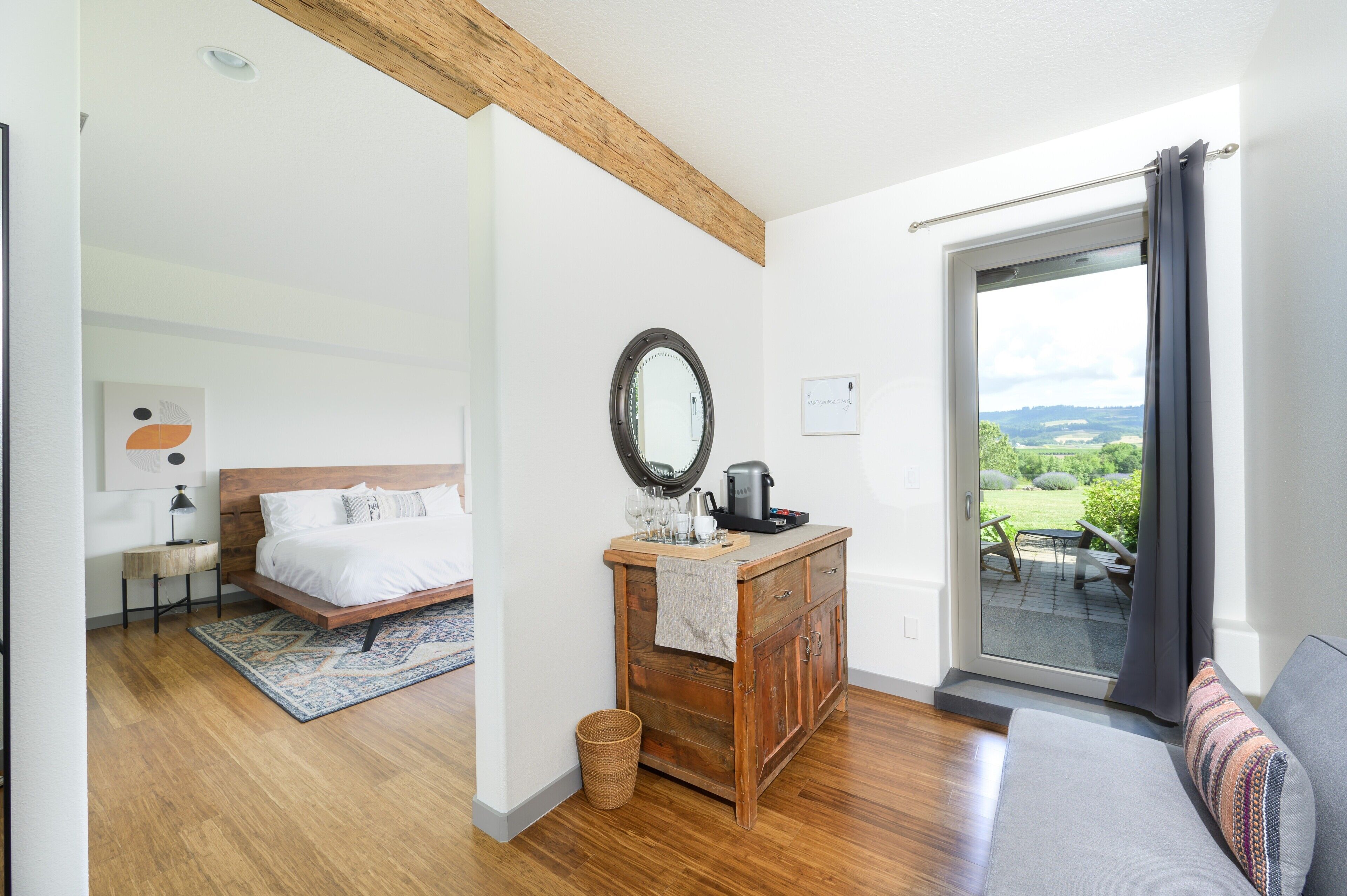 A bedroom with a bed, a wooden dresser, a mirror, and a view of the outdoors through a glass door.