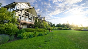 Une maison moderne à deux étages, dotée d’un balcon, entourée d’une végétation luxuriante et d’une pelouse bien entretenue.