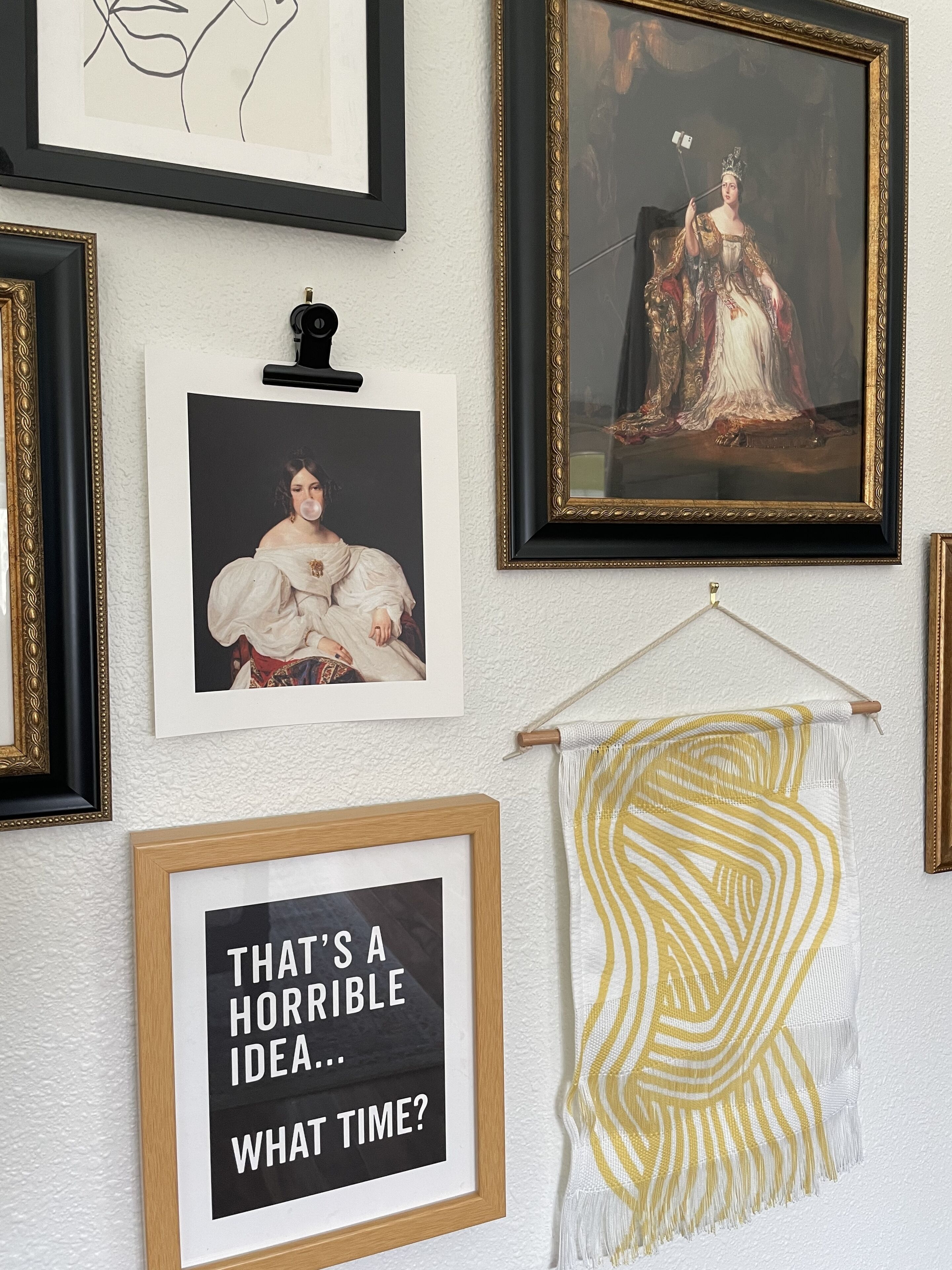 A wall with various framed artworks, including a portrait, a line drawing, and a humorous sign.
