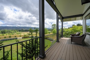 A covered balcony with a view of a green landscape and distant hills.