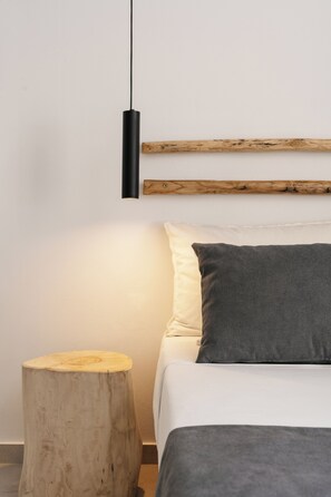 Un dormitorio con cama, mesita de noche de madera, lámpara fijada a la pared y cabecera de madera.