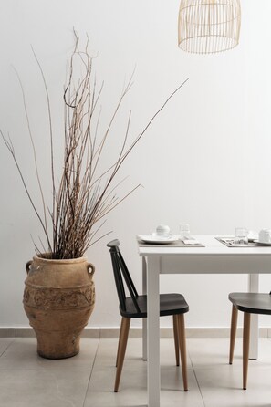 A dining area with a white table, black chairs, a terracotta pot with branches, and a hanging light fixture. - Petradi Beach Lounge Hotel by GHH (Rethymno)