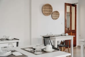 A dining area with a white table set for two, a wooden door, and two woven wall decorations. - Petradi Beach Lounge Hotel by GHH (Rethymno)