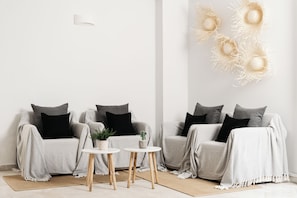 A modern living room with two grey sofas, black cushions, a small round table, and a decorative wall piece. - Petradi Beach Lounge Hotel by GHH (Rethymno)