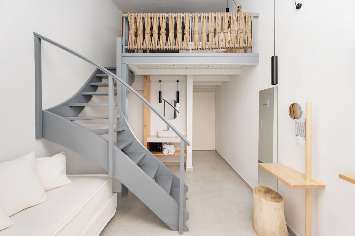 Un interior modern amb una escala espiraltra gris, un sofà blanc, una banca de fusta i un tamboret de fusta petit.