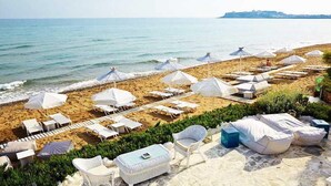 A beachside hotel with rows of sunbeds and umbrellas, a pool area, and a view of the sea.