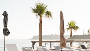 A poolside area with lounge chairs and umbrellas, a wooden deck, and a view of the sea. - Petradi Beach Lounge Hotel by GHH (Rethymno)
