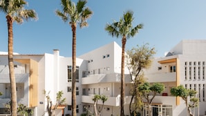 A modern building with multiple balconies and palm trees in front. - Petradi Beach Lounge Hotel by GHH (Rethymno)