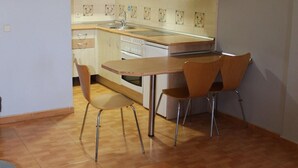 A compact kitchen with a dining area, including a wooden table and chairs, a microwave, and a stove. - Apartahotel Villa De Parla (Parla)