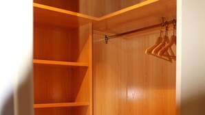 A walk-in closet with wooden shelving, a hanging rod, and a small cabinet. - Apartahotel Villa De Parla (Parla)