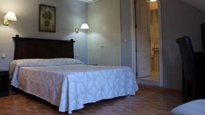 A bedroom with a bed, two wall-mounted lamps, a painting, and a door leading to a bathroom. - Apartahotel Villa De Parla (Parla)