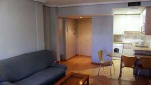 A living room with a sofa, a coffee table, and a dining area with chairs. There is a kitchen in the background. - Apartahotel Villa De Parla (Parla)