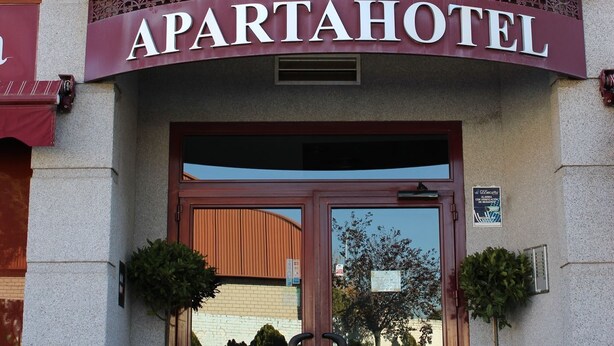 The entrance of an apartha hotel with a sign above the door, potted plants on either side, and flags above. - Apartahotel Villa De Parla (Parla)