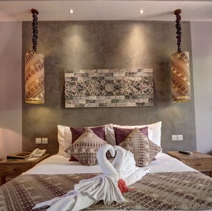 Habitación de hotel con cama, panel decorativo en la pared, lámparas colgantes y teléfono en la mesita de noche.