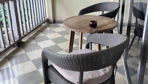 Un balcó amb un paviment de pissos quadriculats, cadires de vimet, una taula rodona de fusta i una petita tassa.