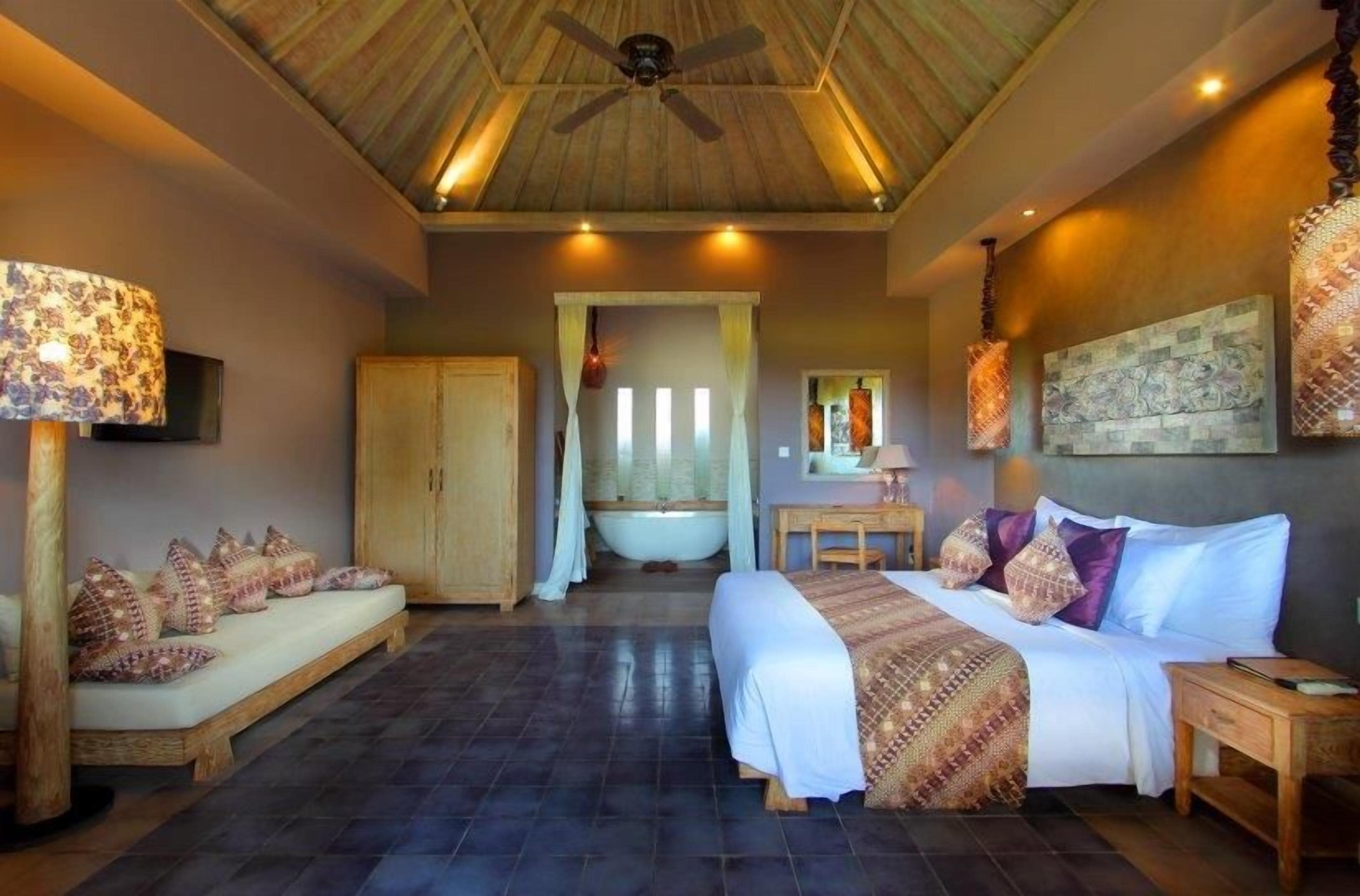 A bedroom with a bed, a sitting area, a bathtub, and a ceiling fan.
