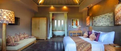 A bedroom with a bed, a sitting area, a bathtub, and a ceiling fan.