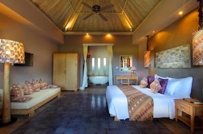 A bedroom with a bed, a sitting area, a bathtub, and a ceiling fan. - Mathis Retreat Ubud (Ubud)