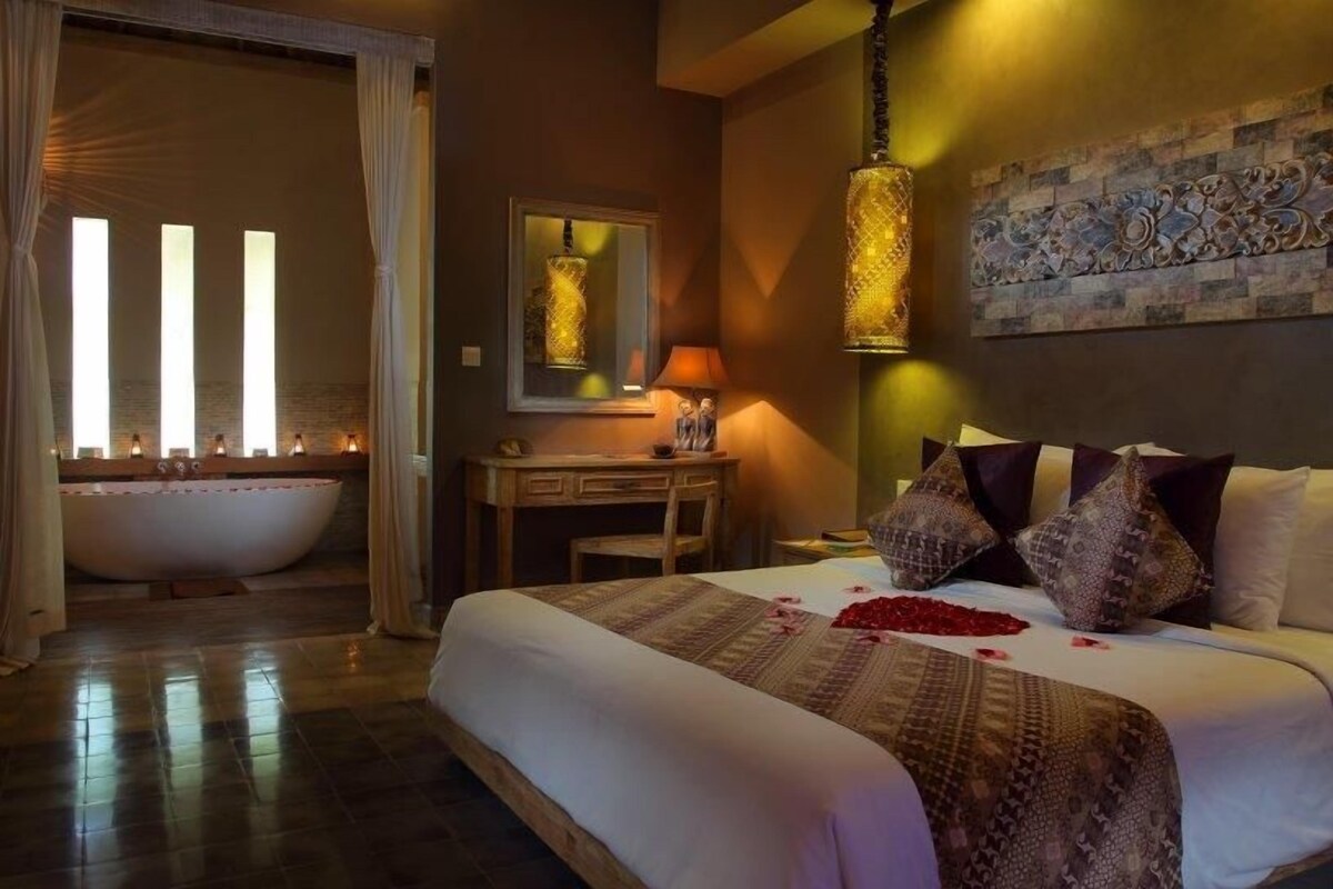 Quarto de hotel com uma cama grande, uma mesa de trabalho, uma banheira e uma parede com detalhes decorativos.