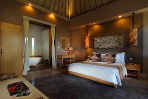 Ein Schlafzimmer mit einem großen Bett, Nachttischen, einem Schreibtisch, einem Sessel, einer Badewanne und einer Duschkabine.