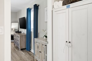 A hallway with a white wardrobe, a TV mounted on the wall, a wooden dresser, and blue curtains.