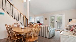 A dining area with a wooden table and chairs, a striped sofa, and a staircase. - Sun Hut: Oceanside Home w/ Private Pool, Short Walk to the Beach! (Corolla)