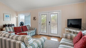 A living room with striped sofas, a television, and a large window with blinds.