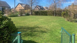 Ein grünes Rasenstück mit einem Zaun, Bäumen und Häusern im Hintergrund.