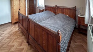 Ein hölzernes Himmelbett mit einem gemusterten Bettbezug, ein Holzschrank und ein kleiner Nachttisch mit Lampe.