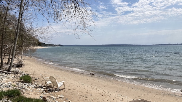 Une plage avec une terrasse en bois, une rangée de chaises blanches et une côte rocheuse.