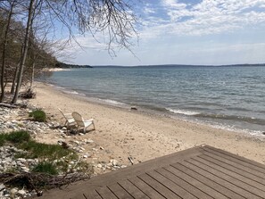 Ein Strand mit einer Holzterrasse, einer Reihe weißer Stühle und einer felsigen Küstenlinie.