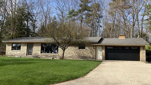 Une maison en pierre avec un garage, une pelouse et des arbres en arrière-plan.