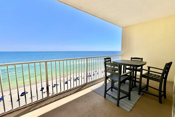 A balcony with a view of the ocean, a table, and chairs.
