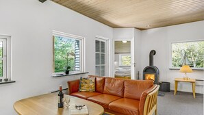 Un salón acogedor con un sofá de cuero, una mesa de madera con una botella y vasos, una chimenea y ventanas con vistas a zonas verdes.
