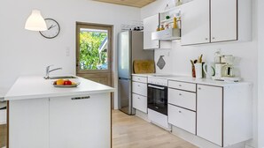 Una cocina moderna con armarios blancos, horno empotrado, lavaplatos y ventana con vistas al verdor.