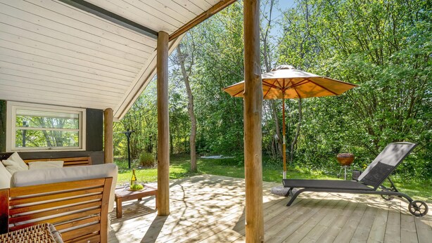 Una terraza de madera con un sofá, una silla de descanso y una mesa con una botella.