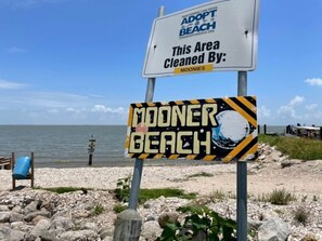 Segnale sulla spiaggia con la scritta 'MOONER BEACH' e un cartello sopra che indica 'Pulito da: MOONIES'.