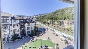 A multi-story building with balconies, a paved courtyard, and a view of a mountainous landscape. - Modern ski in/ski out studio with access to hot tub, fire pit & fire place (Winter Park)