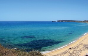 A beach with clear blue water, sandy shore, and a distant rocky coastline.