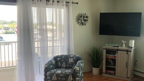 Ein Wohnzimmer mit Holzboden, einem gemusterten Sessel, einem Fernseher, einer Bücherwand und einer Topfpflanze.