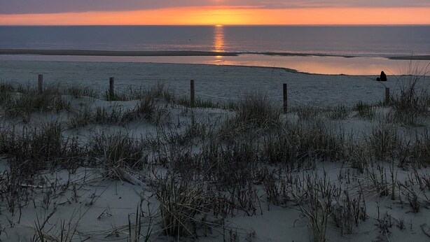 Ein Strand mit Dünen und einem Sonnenuntergang über dem Ozean.