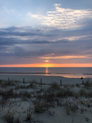 A beach with sand dunes and a sunset over the ocean.