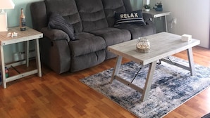 Ein Wohnzimmer mit einem grauen Sofa, einem Holztisch und einem blauen Teppich.