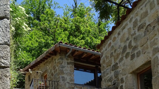 A stone building with a wooden table and chairs, an archway, and a small balcony. - Gite de Chapelèche les Glycines Pour 8 à 10 Personnes (Gluiras)