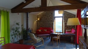 A cozy living room with a stone wall, a red sofa, a wooden table, and a chair. - Gite de Chapelèche les Glycines Pour 8 à 10 Personnes (Gluiras)
